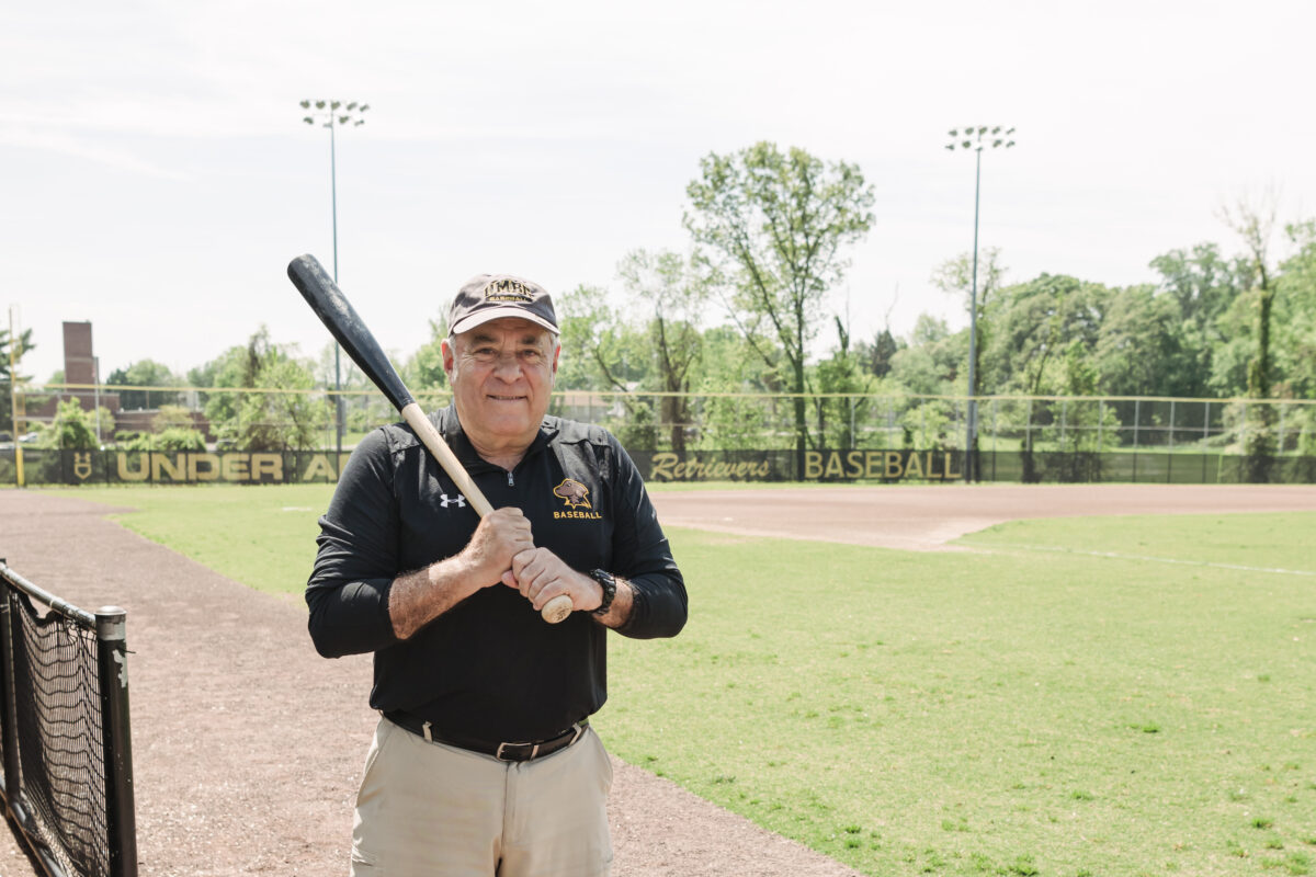 an older man in a black polo shirt stands on a baseball field holding a bat