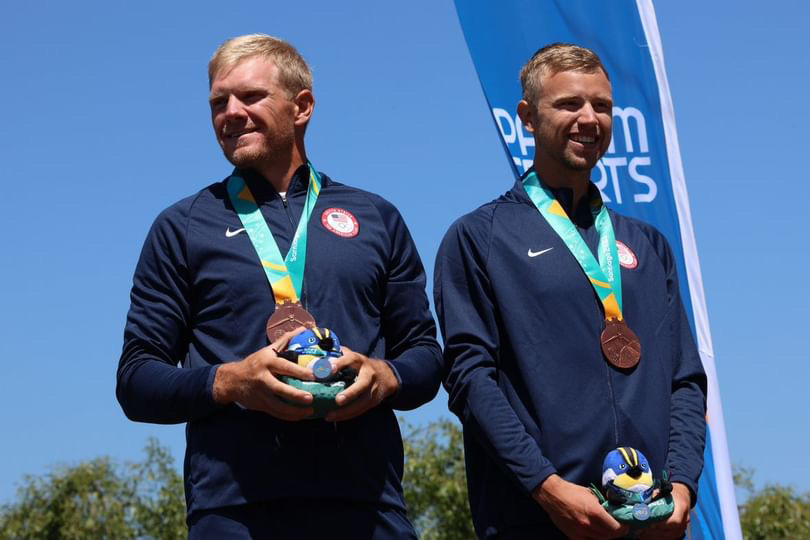 Two men with bronze medals around their necks. They are smiling and holding items in their hands. 