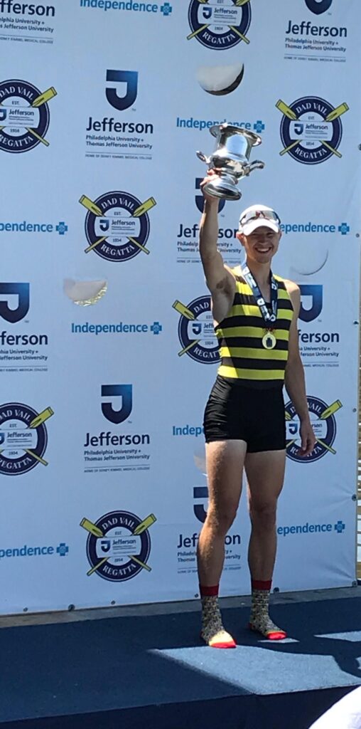 Mark Couwenhoven holding up a trophy and smiling aftering winning the men's single event at the 2019 Dad Vail Regatta. 