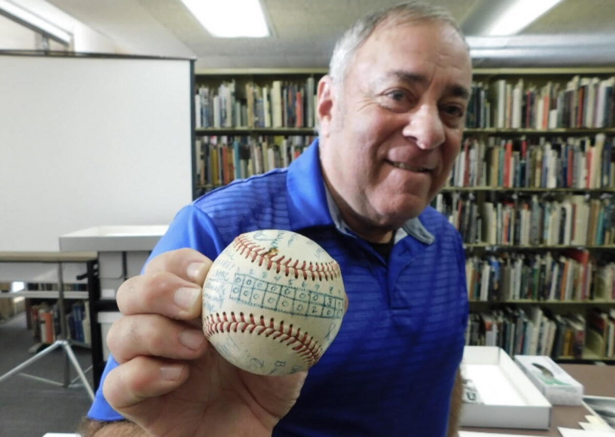 In UMBC's Special Collections, Soracoe holds up the first game-winning baseball with the box score drawn on, a relic of UMBC history