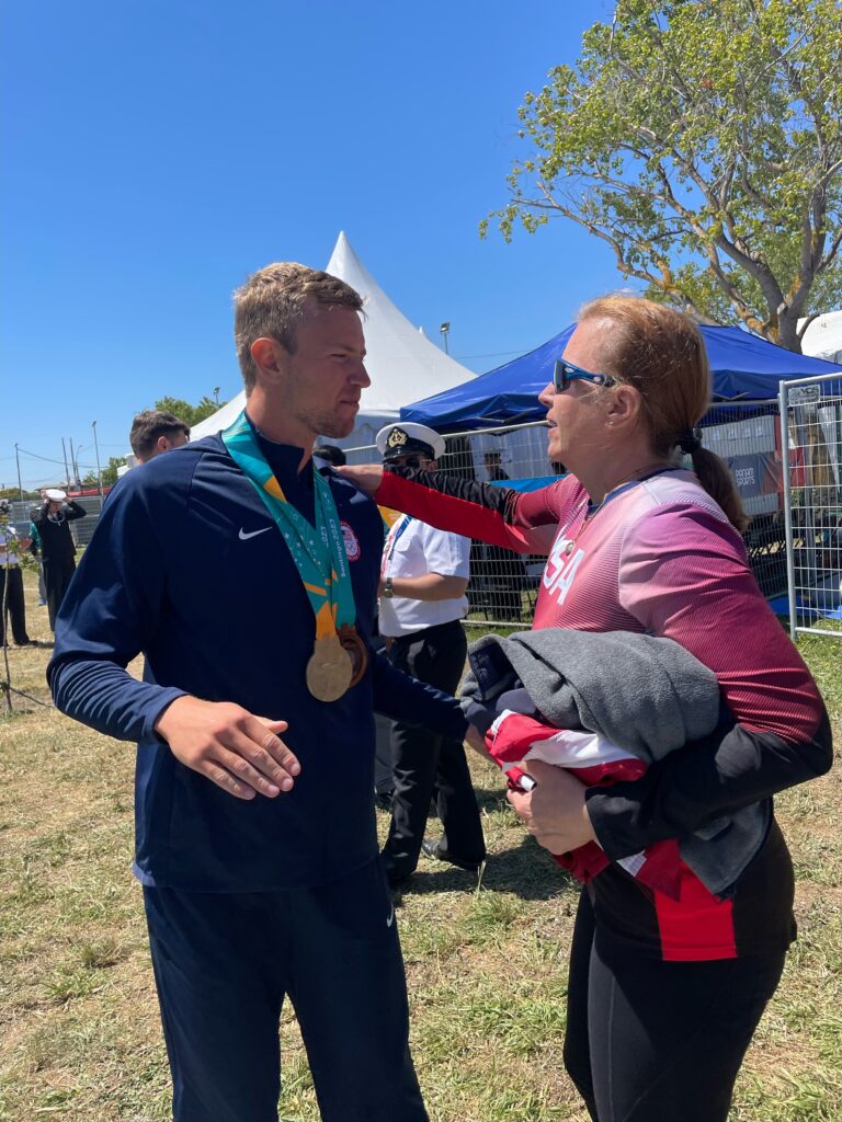 A mother and son about to embrace in a hug. The son is wearing gold and bronze medals around his neck, which he won at the 2023 Pan American Games. 