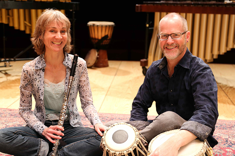 Two seated people pose with musical instruments.