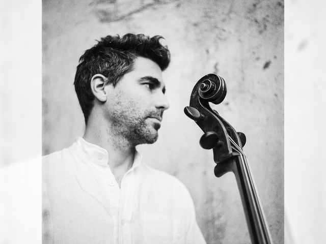 In a black and white image, a man poses with the neck of a cello.