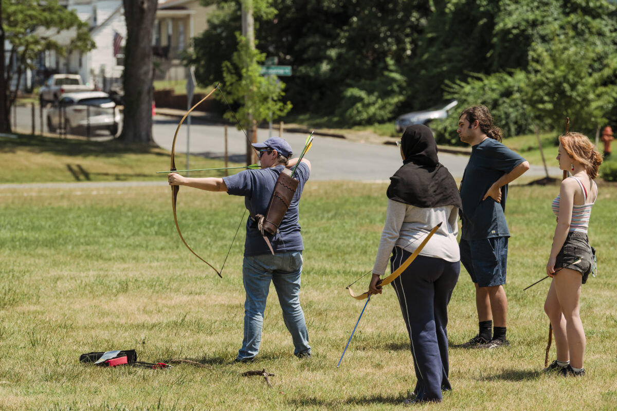 instructor demonstrates use of a bow and arrow to students