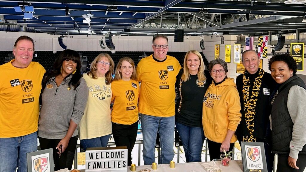 A group of adults in black and gold sportswear pose in an events center.