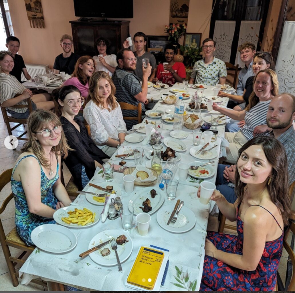 A large group of people sit at a long table having a dinner at a tavern in Greece.