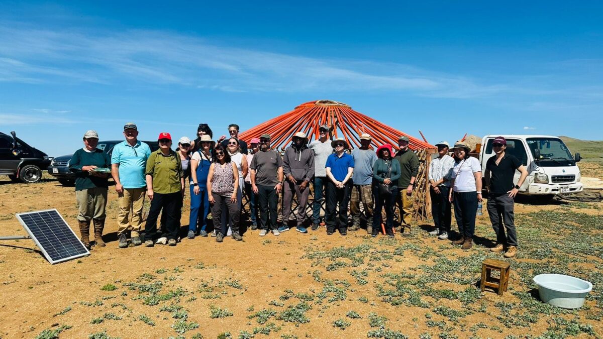 Christopher K. Tong stands with a group of twenty researchers stand in front of a red ger or yurt in Mongollia.