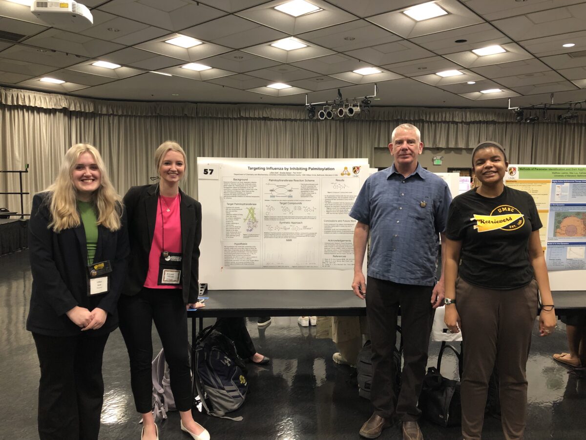 four people standing around a chemistry research poster inside a ballroom