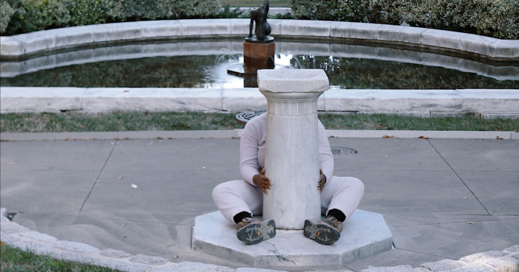 A person, visible only by their arms and legs, is wrapped around a marble pedestal.
