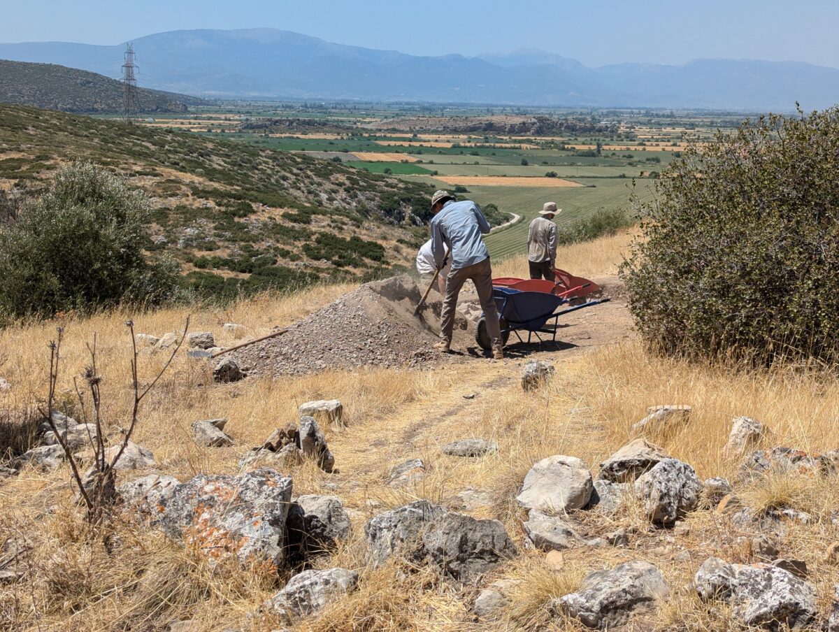 Students in an archaeological site use wheel barrows to carry soil to back fill trenches in Greece