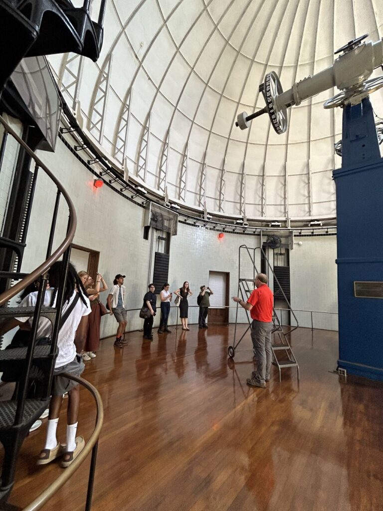 speaker addresses a line of interns inside a large dome with a telescope at the center