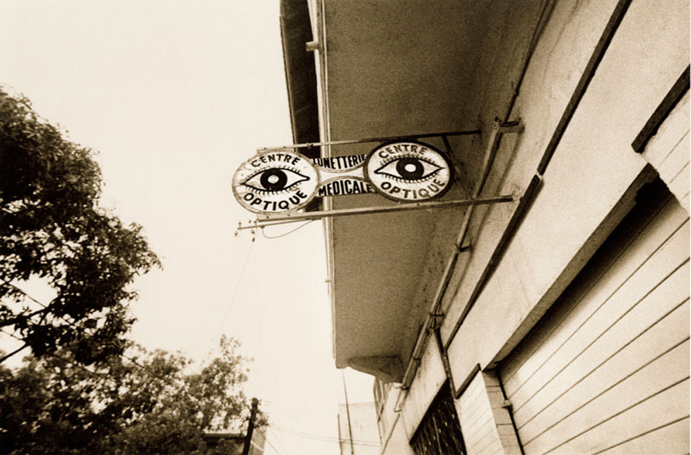 In a sepia-toned photograph by Kerry Coppin, a sign in the shape of a pair of glasses says Centre Optique.