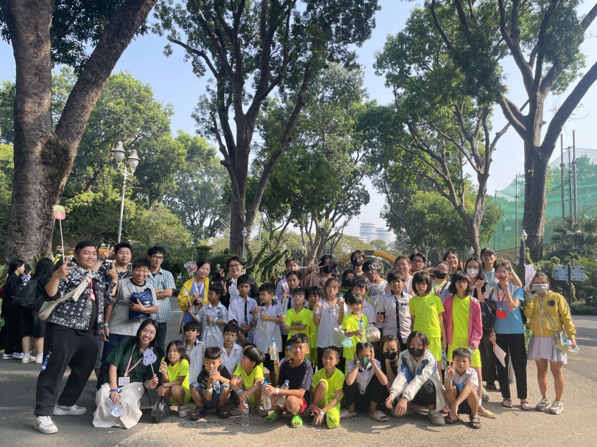 a large group photo of mostly children, several wearing neon green t-shirts, and a few adults stand outdoors backed by trees at the Saigon Zoo