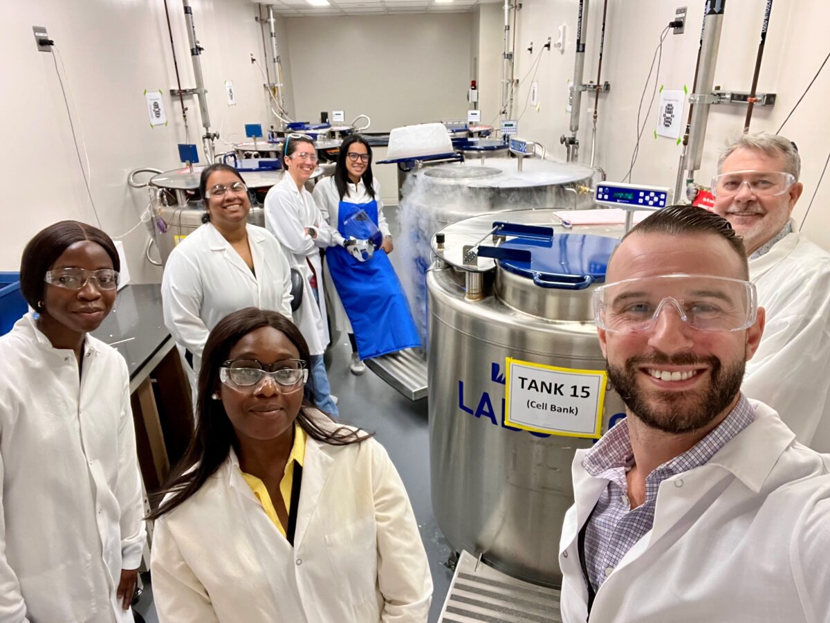 people in white coats stand in a lab with metal tanks in the background