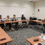 A classroom with tables set up in a circle with SSA/RDRC students listening to a presentation