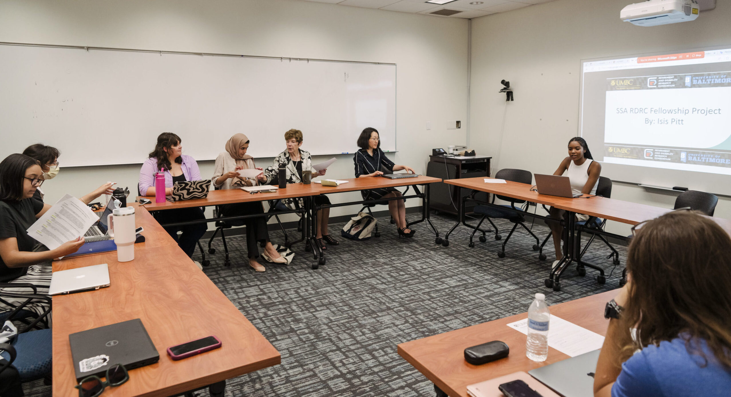 A classroom with tables set up in a circle with SSA/RDRC students listening to a presentation