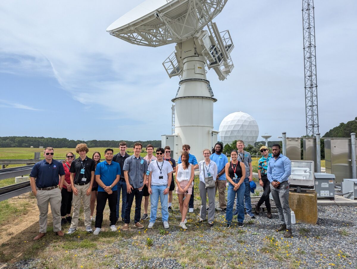 Group of people pose for photo with large telescope in the background.