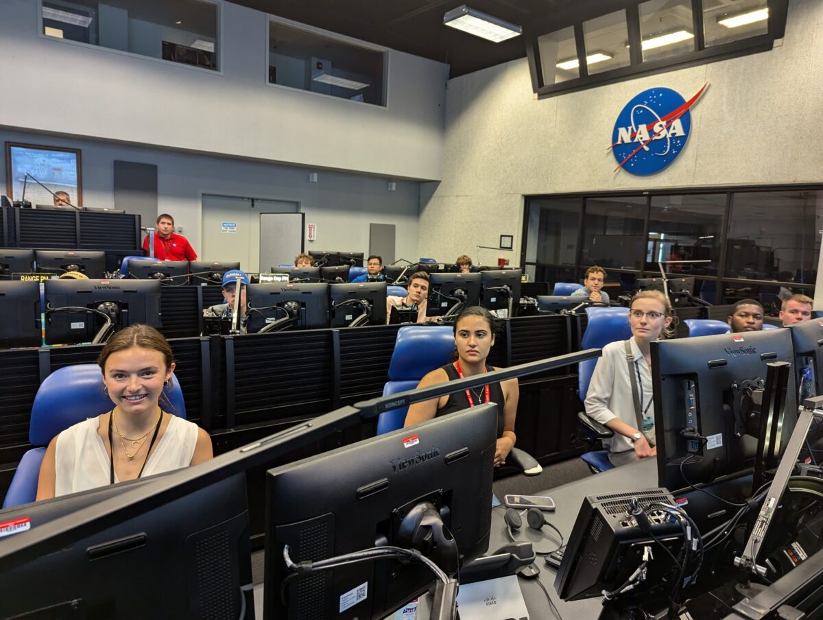 Group of interns sit in large room filled with computers. NASA logo on the wall.