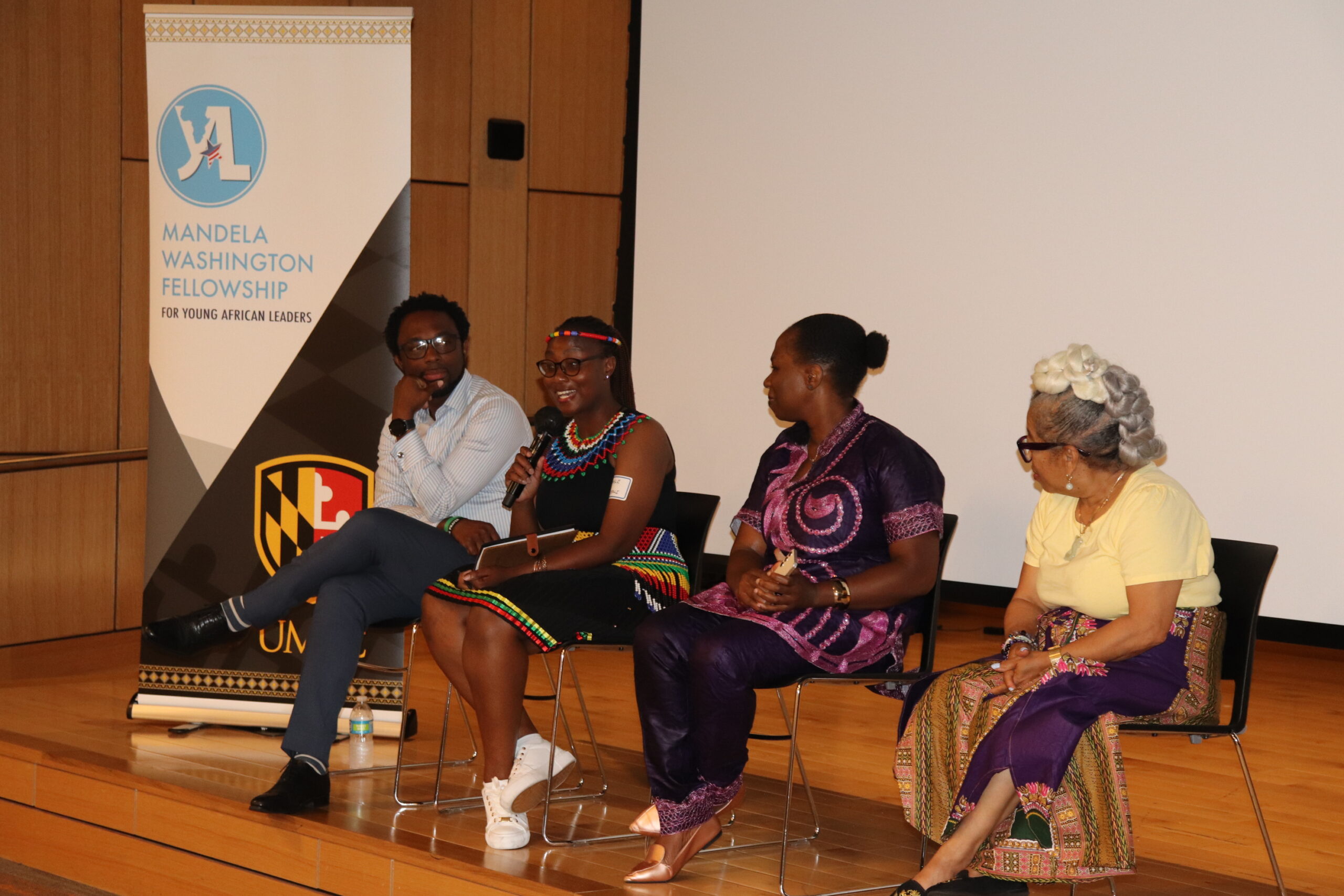 A panel of four young African leaders sit on a stage. Buhlebakhe Shantel Tafadzwa Ncube is holding the microphone.