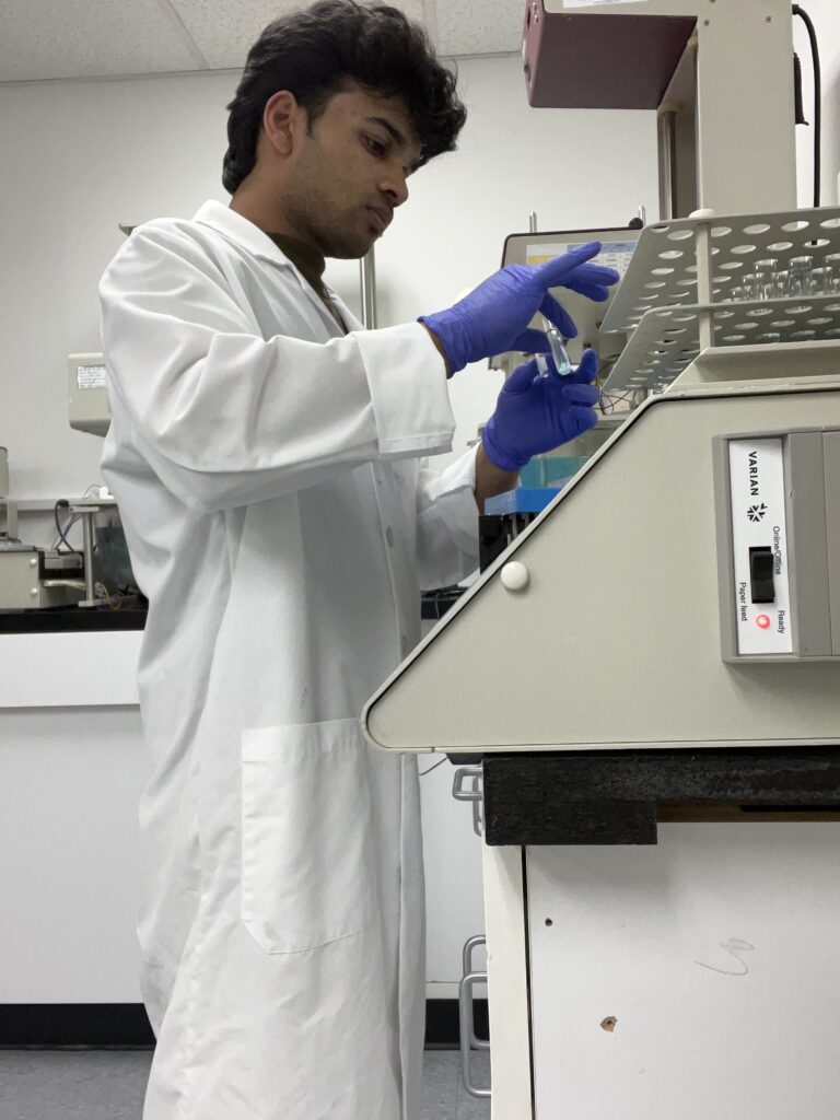 man in white lab coat and purple gloves works at a bench in a biotechnology laboratory