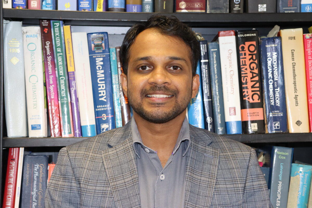 head and shoulders portrait of man; bookshelves of textbooks in the background