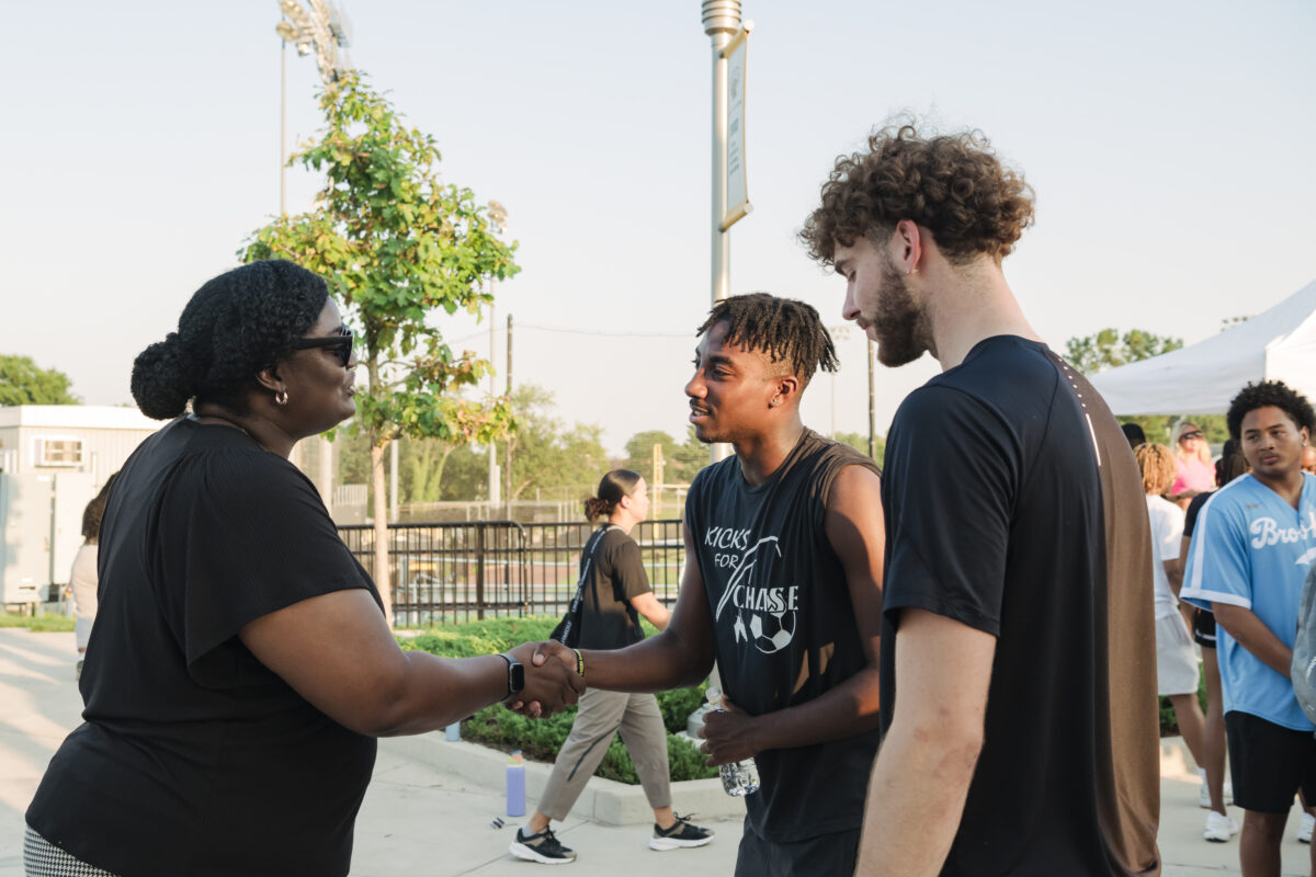 UMBC's athletic director shakes hands with a student athlete while another looks on