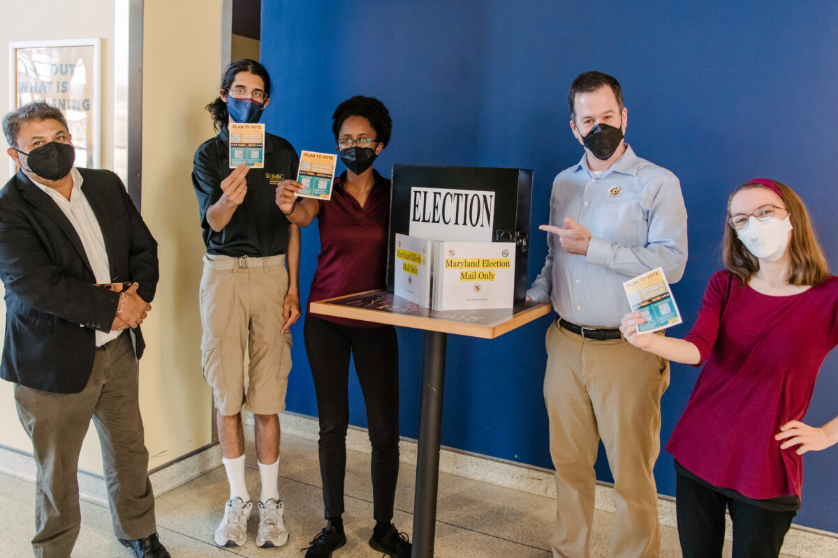 a group of people stand around a ballot box to encourage voters on campus