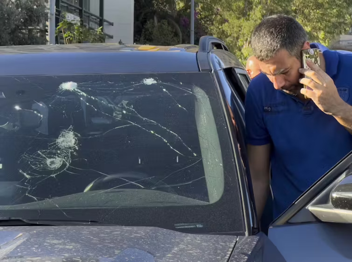 A man on a cell phone stands next to a car with a damaged windshield.