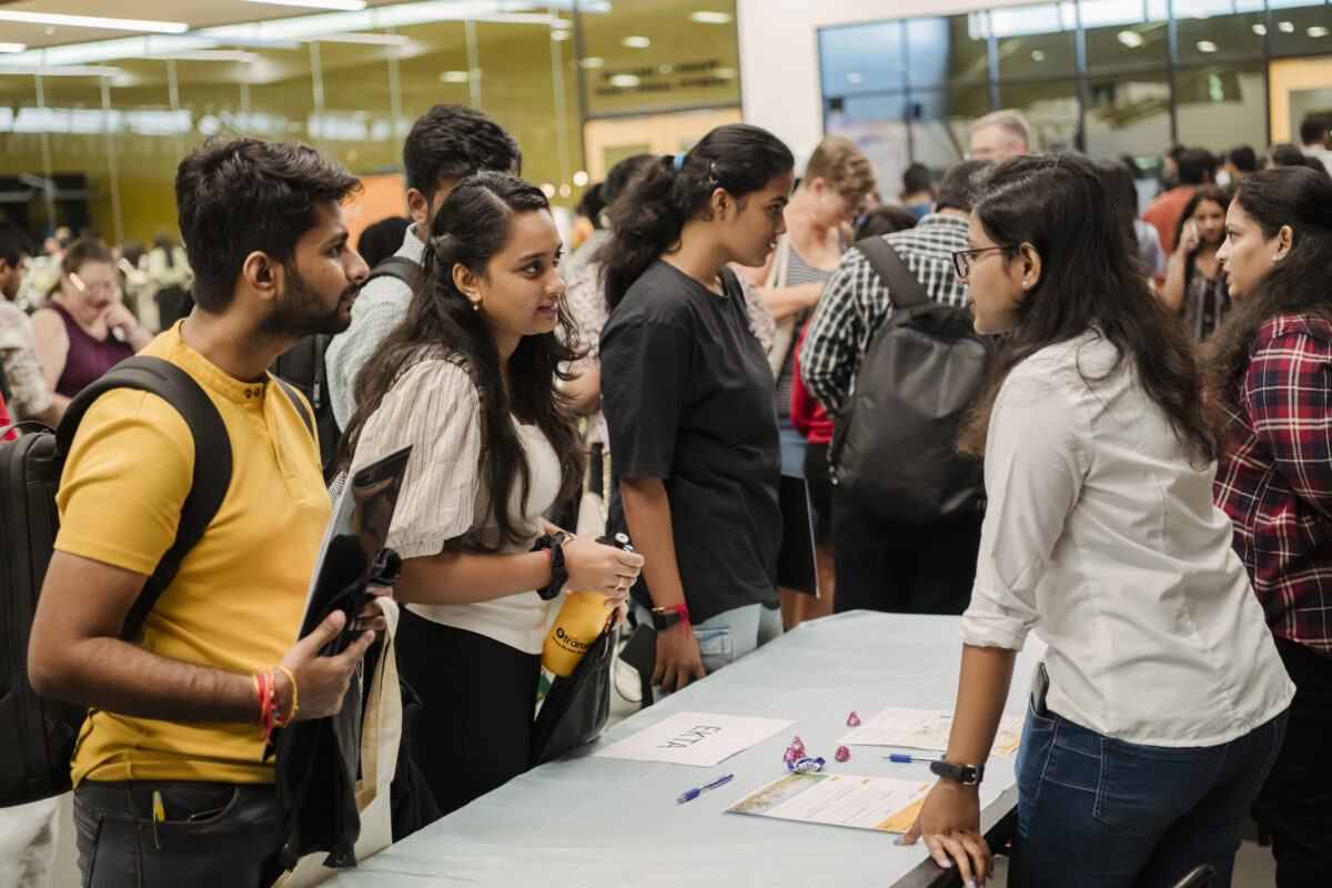 A group of students speak to another student at a table