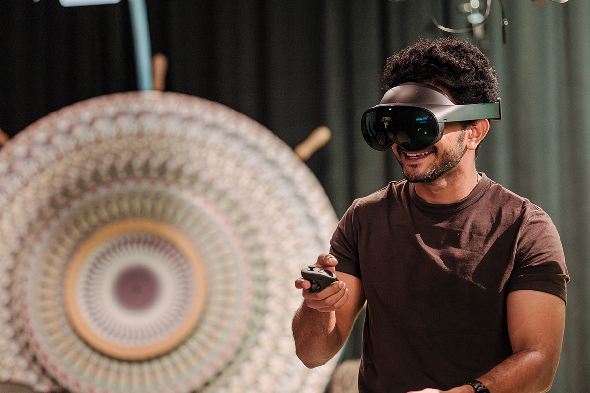 A student wearing VR goggles pointing a remote, and a large spinning mandala in the background