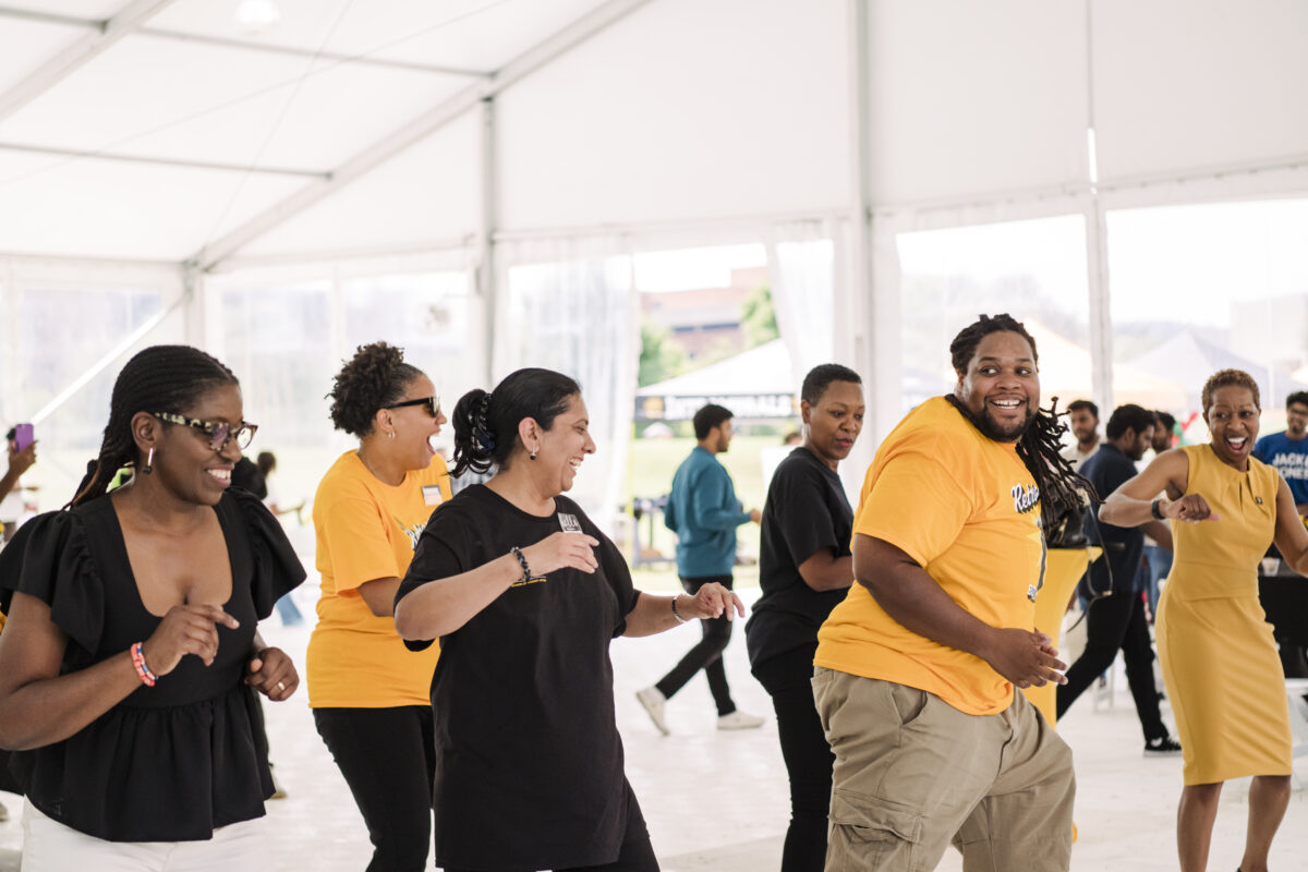 A group of staff members In black and gold are caught dancing