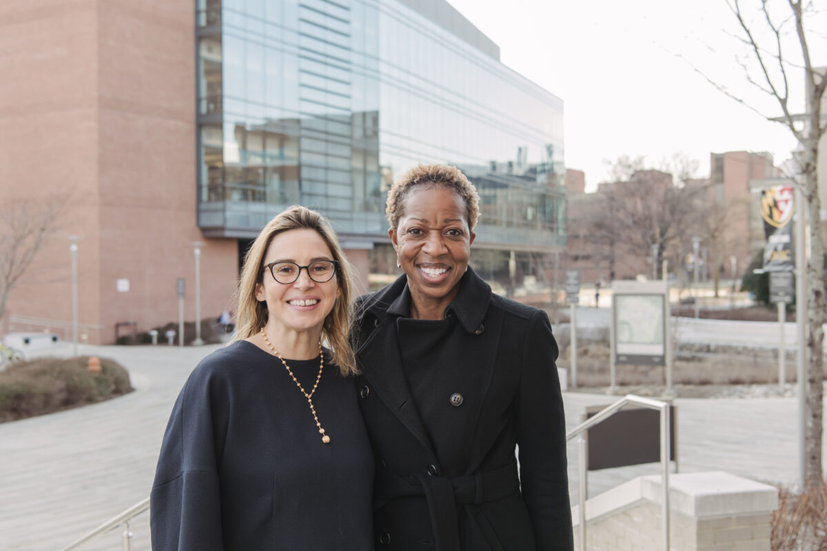 Two women wearing all black smiling at the camera on UMBC's campus.