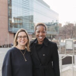 Two women wearing all black smiling at the camera on UMBC's campus.