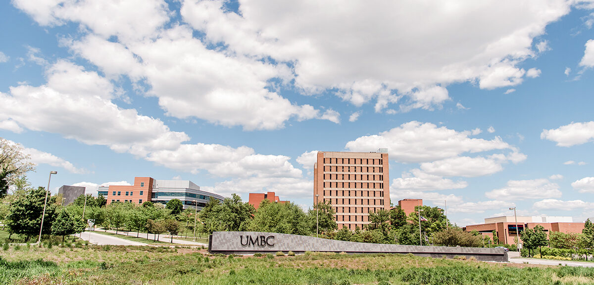 One of the entrances of UMBC's campus. There is a UMBC sign in front of a tall building. The sky is blue and clouds are in the sky. UMBC announces partnership with national nonprofit