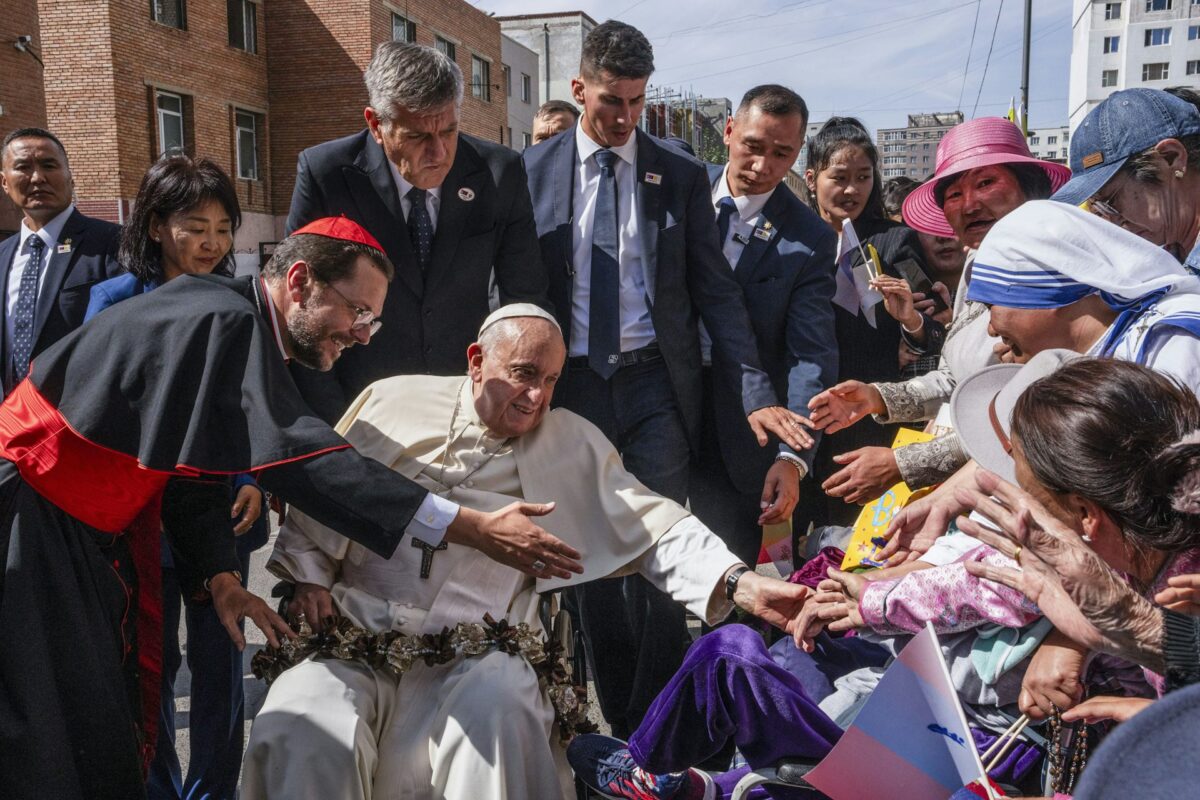 Pope Francis sits in a wheelchair as he greets a crowd of people extending their hands