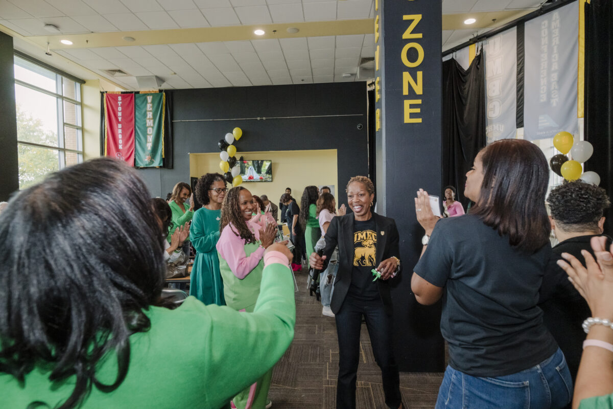 Room full of members of  Alpha Kappa Alpha sorority Lambda Phi chapter. Woman in center is smiling and holding a microphone, which is umbc president valerie sheares ashby.