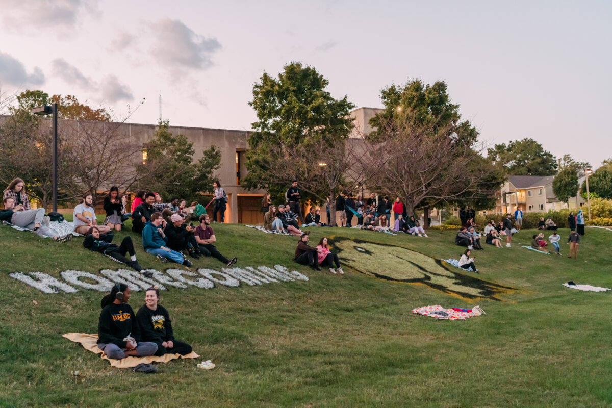 Groups of people gather on lawn. Lawn is painted with word "Homecoming."