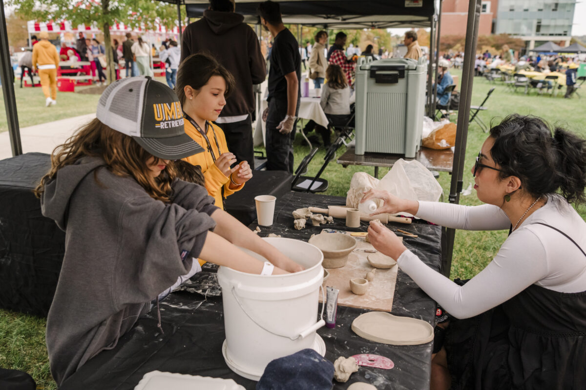 Two children and an adult playing with pottery and ceramics. One child in the front has her hands in a white bucket. 