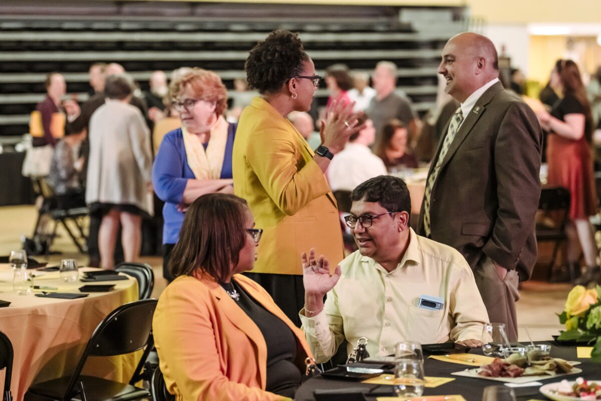 A gym filled with business people speaking to each other Great Colleges to Work For