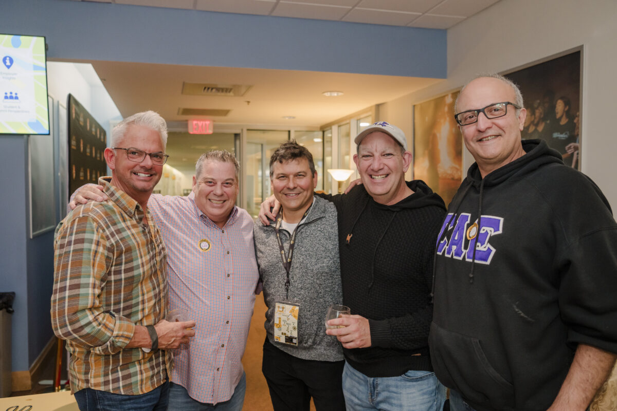 five men smiling for the camera. they all have their arms around each other's shoulders. 