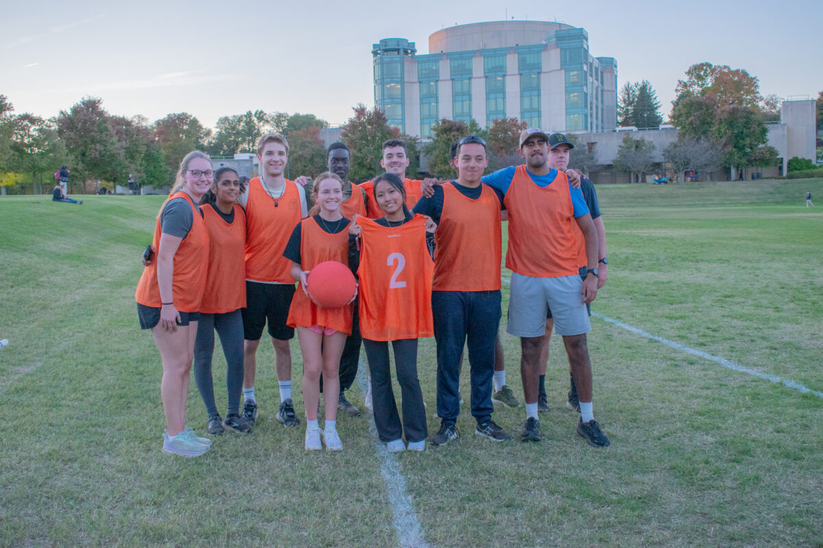 Nine UMBC students wearing orange athletic vests. One student in the center is holder a red kickball. 