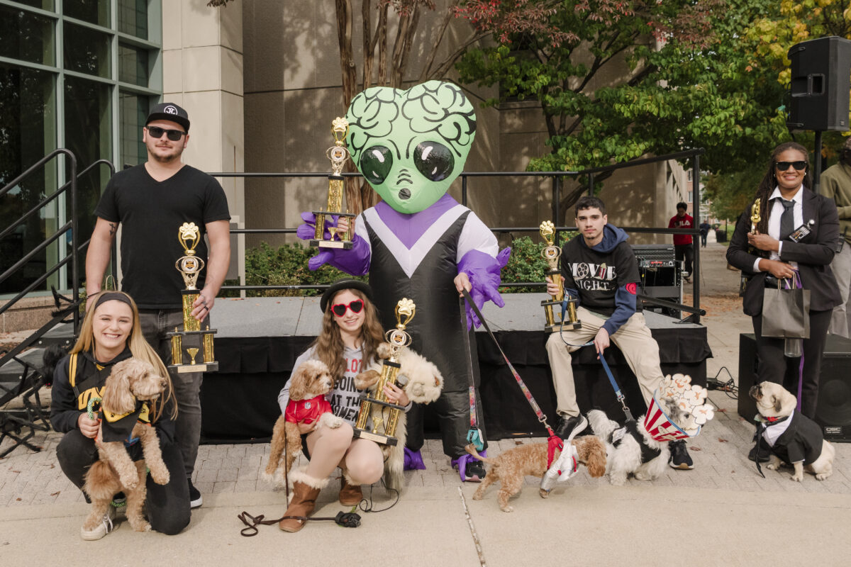 the winners of the 2024 UMBC puppy parade. the winners are holding trophies while dressed in a variety of costumes. the dogs are also wearing costumes as well 