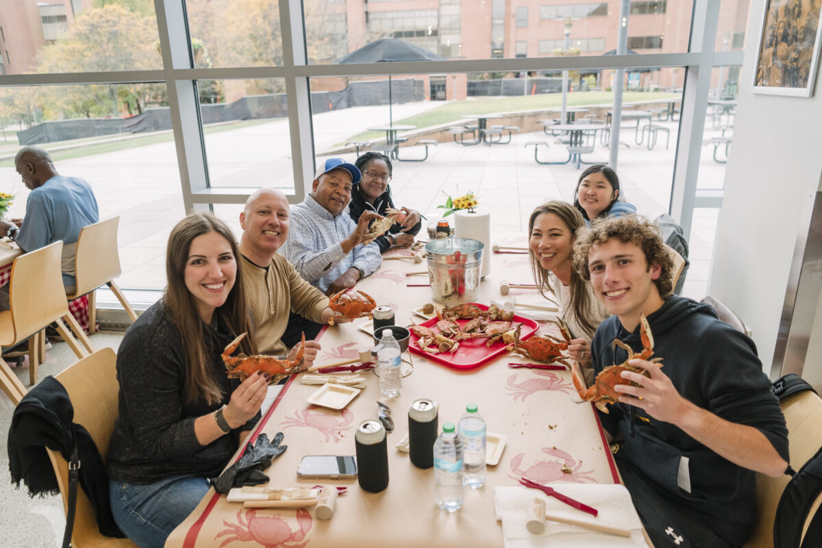 a large table of umbc homecoming attendees holding crabs/ they are sitting at a table outfitted with crabs, drinks, utensils, and more. 