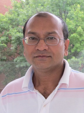 Man with light pink and white collared shirt that has a faint blue line right below collar of shirt. he is wearing oval rectangular glasses. 