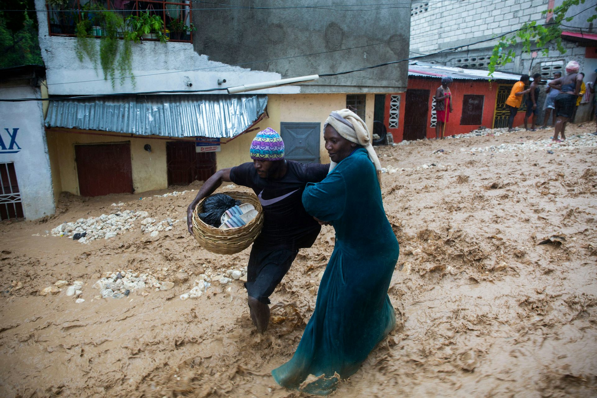 Two people in the Caribbean carrying a basket of clothes run from an overflowing river after a hurricane due to legacy of colonialism