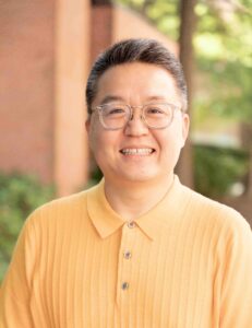 headshot of a man in glasses with a yellow button up shirt