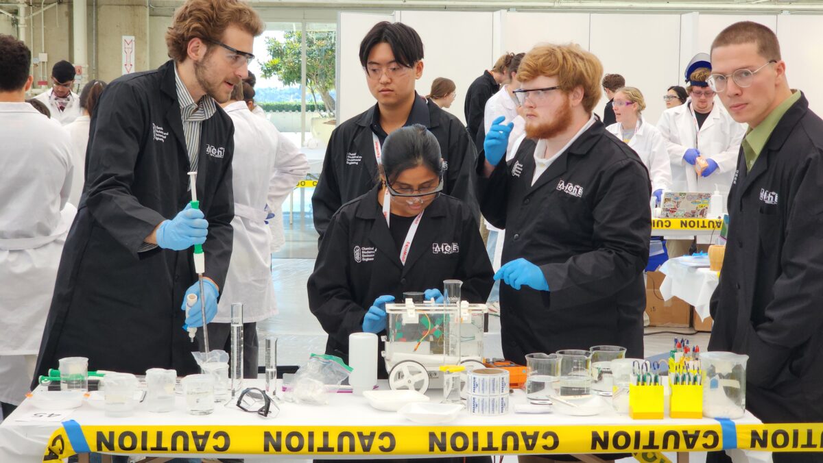 Student in black lab coat work with chemical equipment on a table.