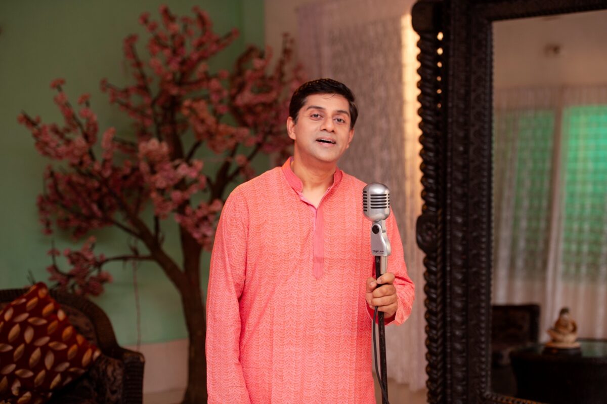 A man of Bengali descent is holding the stand of an old fashion microphone. he has his mouth open and looks like he is preparing to sing. 