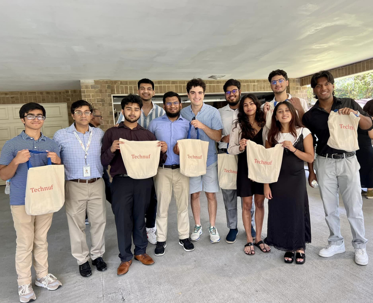 A group of 11 people posing for a picture. the group of 10 students are holding beige tote bags that say technuf on it. 