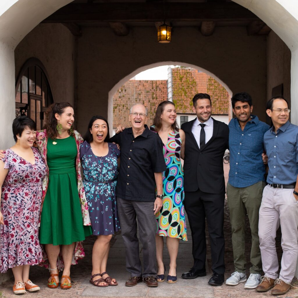 group photo of eight people dressed nicely under an outdoor arched breezeway